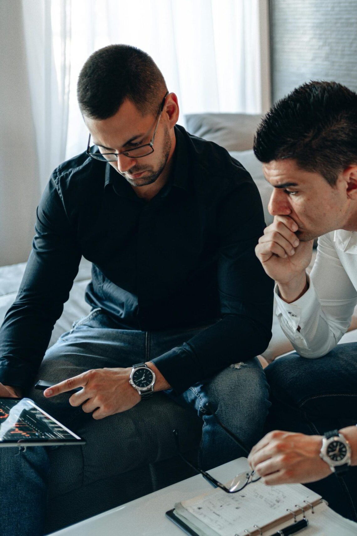 Two men discussing market trends using a tablet in an office setting.